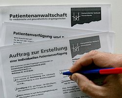 Eine Hand eines Patienten füllt einen Antrag auf eine Patientenverfügung aus.