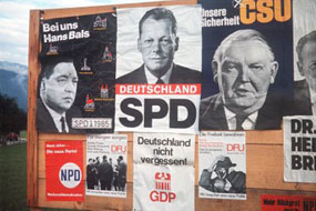 Wahlplakate fr die Bundestagswahl 1965 kleben auf einer Holzwand an einer Strae.