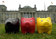 3 Sparschweine auf einer Wiese vor dem Reichstagsgebäude