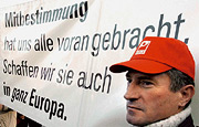 Bild: Demonstrant mit Plakat. Auf dem Plakat steht: Mitbestimmung hat uns alle vorangebracht. Schaffen wir sie auch in ganz Europa.