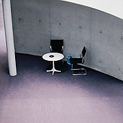 Bild: Zwei Stühle und Tisch vor Betonwand.