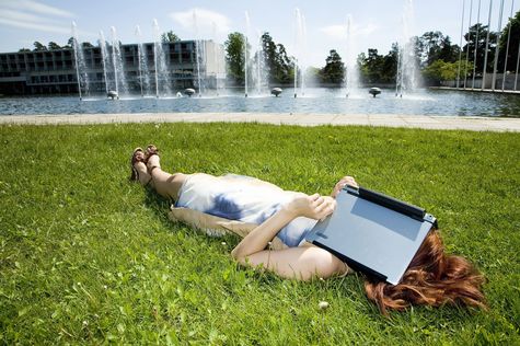 Frau schützt ihr Gesicht mit einem Laptop vor der Sonne