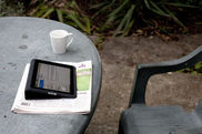 Tablet, Zeitung und Kaffeetasse auf einem Gartentisch