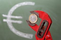 Euromünze in einer Zange eingespannt und Euro-Zeichen