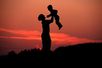 Eine Mutter hebt vor dem rot gefärbten Abendhimmel ihr Kind hoch