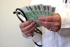 Ein Arzt hält ein Stetoskop sowie etliche 100-Euro-Scheine in der Hand.