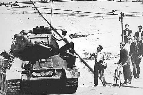 Eine Gruppe von Menschen beobachtet einen russischen Panzer, den ein junger Mann erklettert hat. 