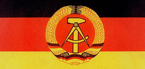 The black, red and gold flag of the GDR bearing the state emblem of a hammer and a pair of compasses inside a wreath of wheat ears.