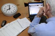 Mann arbeitet am Computer, daneben eine Uhr