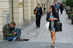 Eine  Frau mit Sonnenbrille läuft vorbei an einem Bettler.