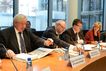 Drei Herren in Anzügen sitzen am Tisch des Ausschusssaales. Der Herr ganz links greift zum Tischmikrofon, von ganz rechts  blickt die Ausschussvorsitzende herüber.