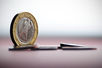 eine Ein-Euro-Münze stehend, davor liegen weitere Münzen