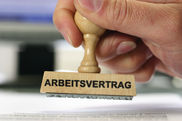 Eine Hand hält einen Stempel. Die Aufschrift des Stempels lautet: Arbeitsvertrag.