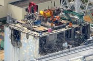 Eine Luftaufnahme auf den zerstörten Reaktor von Fukushima. Auf dem Dach stehen schwere Maschinen, ein Bagger und ein Kran.