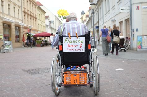 Ein alter Flaschensammler im Rollstuhl in einer Fußgängerzone.  