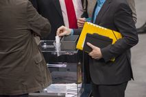 Ein Abgeordneter steckt seinen Wahlzettel in eine gläserne Wahlurne.