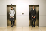 Eine Frau und ein Mann stehen nebeneinander, jeder vor einer verschlossenen Aufzugstür. - Video ansehen... - Öffnet neues Fenster