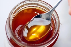 Honig wird aus einem Glas auf einen Löffel genommen