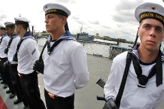 Marinesoldaten in blau-weißen Uniformen stehen in Reihe auf einem Schiffsdeck.