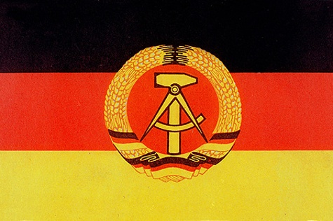 Die schwarz-rot-goldene DDR-Fahne mit dem Emblem, das Hammer und Zirkel im Ährenkranz zeigt.