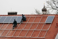 Arbeiter installieren Solarzellen auf einem Dach.