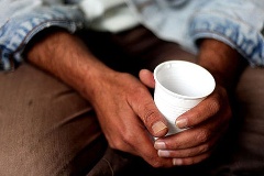 Iranischer Flüchtling hält in seinem Zimmer im Asylbewerberwohnheim einen Plastikbecher mit Wasser in der Hand.