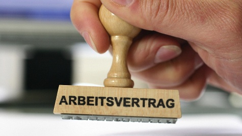 Eine Hand hält einen Stempel. Die Aufschrift des Stempels lautet: Arbeitsvertrag.