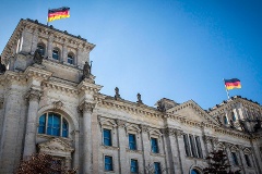 Das Reichstagsgebäude von außen. Auf den Türmen wehen Deutschlandfahnen im Wind.