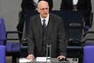 Norbert Lammert spricht stehend vom Platz des Bundestagspräsidenten. Er trägt einen schwarzen Anzug mit Weste, ein weißes Hemd und eine dunkle Krawatte.