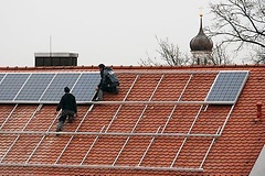 Arbeiter installieren Solarzellen auf einem Dach.