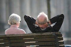 Ein Rentnerpaar von hinten auf einer Bank sitzend. Der Mann rechts hat die Arme hinter dem Kopf verschränkt.