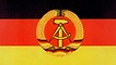 Die schwarz-rot-goldene DDR-Fahne mit dem Emblem, das Hammer und Zirkel im Ährenkranz zeigt.