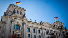 Das Reichstagsgebäude von außen. Auf den Türmen wehen Deutschlandfahnen im Wind.