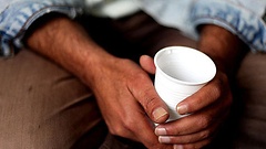 Iranischer Flüchtling hält in seinem Zimmer im Asylbewerberwohnheim einen Plastikbecher mit Wasser in der Hand.