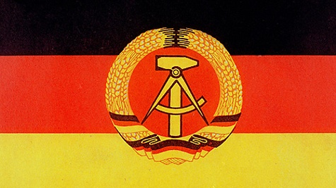 Die schwarz-rot-goldene DDR-Fahne mit dem Emblem, das Hammer und Zirkel im Ährenkranz zeigt.