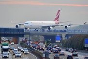 Ein Flugzeug quert auf einer Brücke eine stark befahrene Autobahn.