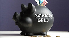 Euro-Scheine im Schlitz eines schwarzen Sparschweins mit der Aufschrift Schwarzgeld.