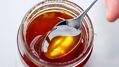 Honig wird aus einem Glas auf einen Löffel genommen