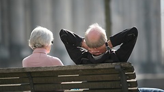 Ein Rentnerpaar von hinten auf einer Bank sitzend. Der Mann rechts hat die Arme hinter dem Kopf verschränkt.