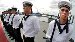 Marinesoldaten in blau-weißen Uniformen stehen in Reihe auf einem Schiffsdeck.