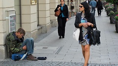 Eine hübsche Frau mit Sonnenbrille läuft vorbei an einem Bettler.