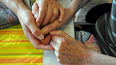 Eine Altenpflegerin hält die Hände einer alten Frau.