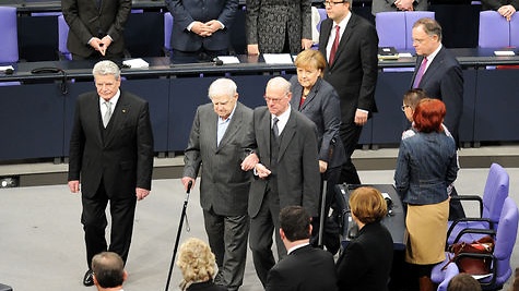 Daniil Granin betritt unterhakt bei Norbert Lammert und mit der rechten Hand auf einen Stock gestützt den Plenarsaal. Links daneben Gauck, dahinter Merkel, Vosskuhle und Weil.