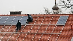 Arbeiter installieren Solarzellen auf einem Dach.