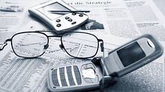 Handy, Brille und Organizer liegen ausgebreitet auf dem Wirtschaftsteil einer Zeitung.